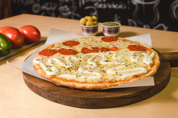 Close-up of a pepperoni pizza and lots of mozzarella cheese next to vegetables on top of a wooden table.