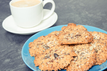 Cup of white coffee and fresh baked oatmeal cookies with honey and healthy seeds. Delicious crunchy dessert