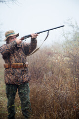 hunter man with a gray beard in hunter suit makes aiming wiring with a double-barreled rifle 