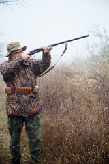 hunter man with a gray beard in hunter suit makes aiming wiring with a double-barreled rifle 