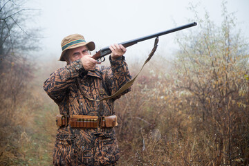 hunter man with a gray beard in hunter suit makes aiming wiring with a double-barreled rifle 