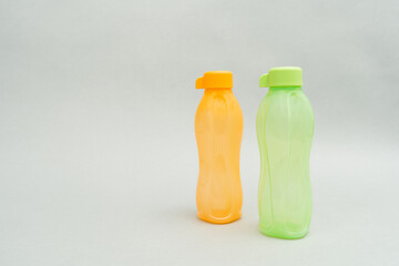 Plastic Tupperware Bottles. Two identical bottles, orange and the back and green at the front and grey on a background.