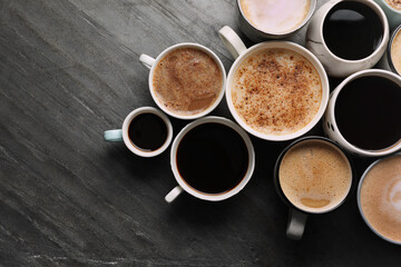 Many cups of different coffees on slate table, flat lay. Space for text