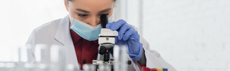 young scientist in medical mask and latex glove looking through microscope in laboratory, banner.