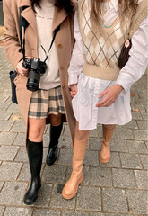 Portrait of two unrecognizable friends walking hand in hand outdoors with fall-winter clothing looks while one holds a camera to take photos of the trip.