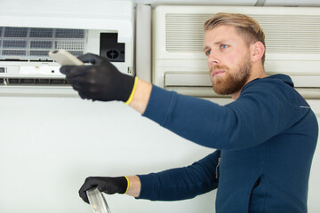 Naklejka na ściany i meble electrician man is fixing the heavy air conditioner