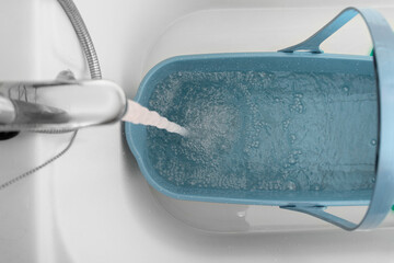 clean water from the tap in the bathroom is poured into a blue bucket for cleaning and mopping...