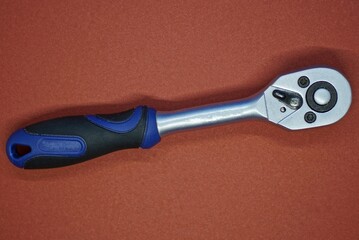 the tool of one gray metal ratchet wrench with a blue black plastic handle lies on a brown table