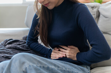 Healthcare medical or daily life concept : Close up stomach of young lady have a stomachache or menstruation pain sitting on her sofa.
