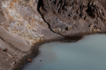A man stands in shallow water along the shore of a geothermal crater lake found in Askja Caldera in the Central Highlands of Iceland.
