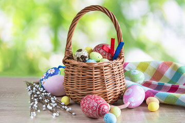 Easter holiday greeting card; Wicker basket with easter eggs, checkered napkin on wooden table against the green natural background