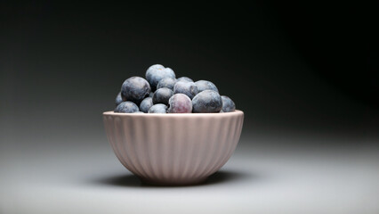 Small pink pot of fresh blueberries with dark background and shadows