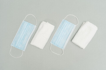 Medical blue surgical masks and white towels on grey background. Protect from the Covid 19 virus during the pandemic and keep yourself clean and maintain good hygiene.