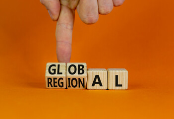 Regional or global symbol. Businessman turns wooden cubes and changes the word 'regional' to 'global'. Beautiful orange table, orange background. Business and regional or global concept. Copy space. - obrazy, fototapety, plakaty