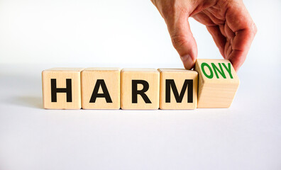 From harm to harmony. Businessman turns the wooden cube and changes word harm to harmony. Beautiful white table, white background. Business and harm or harmony concept. Copy space.