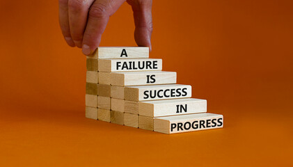 Failure or success symbol. Wooden blocks with words A failure is success in progress. Beautiful orange background, copy space. Businessman hand. Business, failure or success concept.