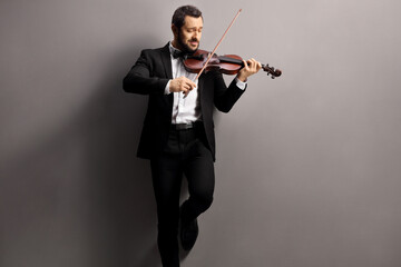 Elegant man playing a violin and leaning on a gray wall