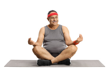 Smiling mature man sitting on an exercise mat and practicing yoga and meditation