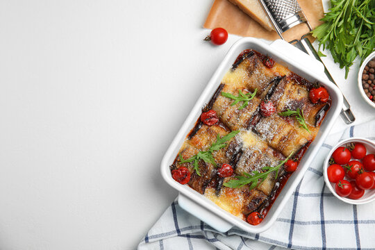 Tasty eggplant rolls with tomatoes, cheese and arugula in baking dish on white table, flat lay. Space for text