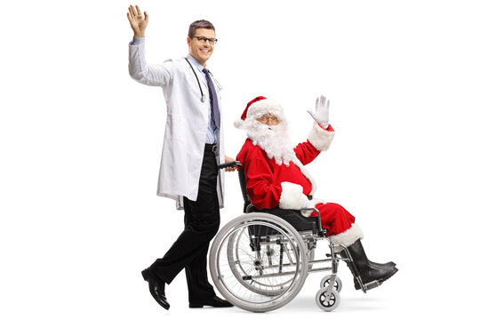 Full Length Profile Shot Of A Doctor Pushing Santa Claus In A Wheelchair And Waving At Camera