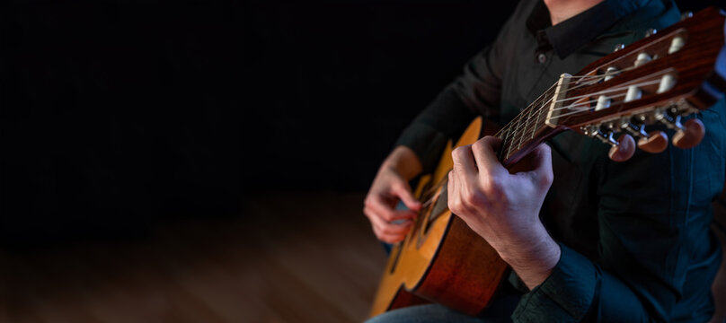 The guy in the dark shirt is plucking the strings of a six-string guitar
