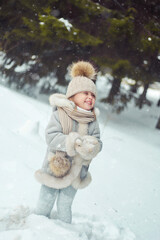 Little beautiful girl in a hat in the winter forest stands in the snow and catches snowflakes. Little girl having fun on winter day,