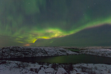 Fototapeta na wymiar Rocks and a lake in winter, the northern lights in the sky.