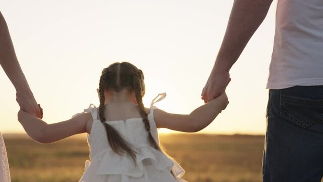 little kid holds his father and mother by hand at sunset, happy family, have fun and play with parents in park, good child life with kind mom and dad, fantasy childhood dream, baby open air of nature