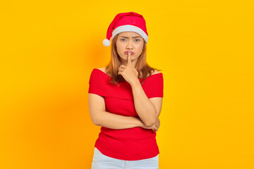 Attractive young Asian woman wearing christmas hat and making silence gesture on yellow background