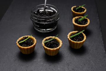 a traditional Russian dish - tartlets with black beluga caviar, decorated with green onion feathers