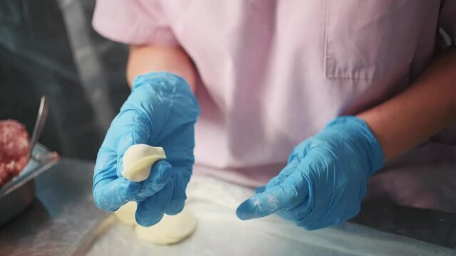 Production in the food shop. Clip. A woman in a special apron and gloves makes dumplings on a special iron table.