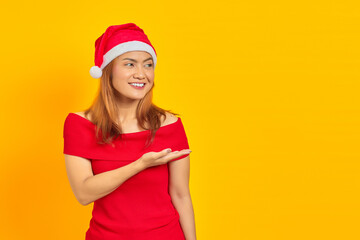 Smiling young Asian woman wearing a christmas hat and extending hand to the side inviting to come