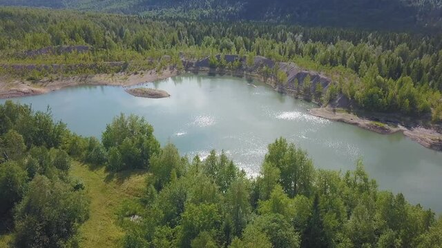 A beautiful blue lake. View from the drone Clip. A small lake next to which are green sunny trees, behind the forest and mountains and clear sky.