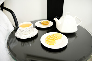 Served table with lemon slices on a saucer, bowl with honey, teacup and teapot with herbal tea in luxury privacy room of wellness spa center