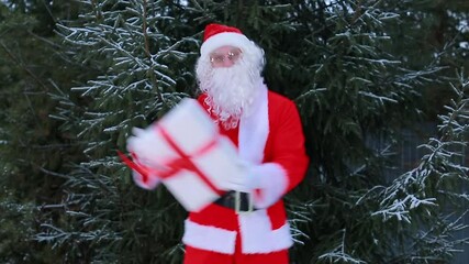 A man Santa Claus is having fun at the Christmas tree with a box of gifts. Merry Christmas