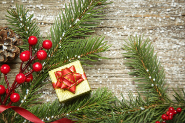 Christmas tree branches, gift box, conifer cones and red berries top view with copy space on old wooden background. Christmas, winter holiday, new year concept.