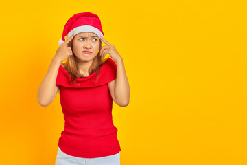 Portrait of a pensive young woman wearing Christmas hat having doubts and thinking on yellow background