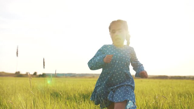 Girl run in field on green grass. Happy child plays and dream. Girl in flower garden.Happy child run towards dream on green grass. Girl playing on flower field in garden.Children fun and joy in summer