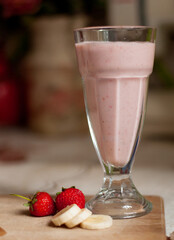 pink cocktail in a glass with strawberries and banana on the background
