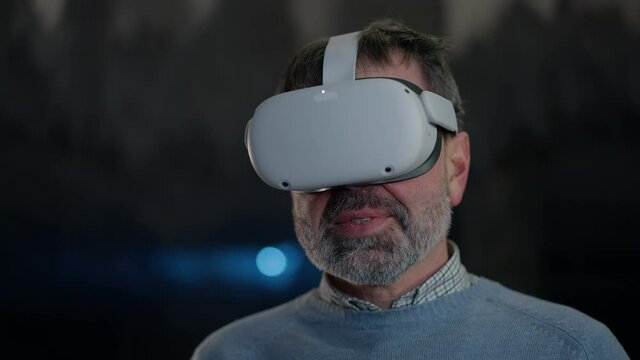 Close-up man in VR headset looking around standing in snow cave with stalactites at background. Portrait of confident male Caucasian explorer enjoying virtual reality outdoors with snow frost around