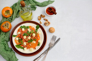 Mix of persimmon, cheese, arugula and walnuts on a plate on a light background. Healthy and healthy breakfast. Top view, copy space