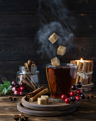 Fototapeta na wymiar Hot tea with cinnamon and berries on wooden saucers. Pieces of cane sugar fly into the cup. Cinnamon tubes in a glass jar and a candle in the background