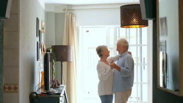 Romantic loving senior couple holding hands enjoying dancing together in the living room of house. Elderly happy couple celebrating by dancing in living room.
