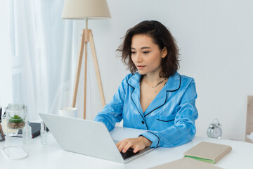 focused young freelancer using laptop near cup and books.