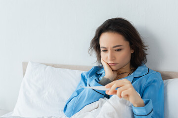 sick young woman looking at electronic thermometer.