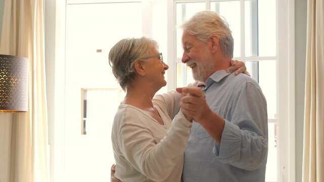 Happy and funny couple of old and mature people having fun and enjoying at home doing a party together singing and dancing playing the guitar indoor. Holiday or event celebrating concept.
