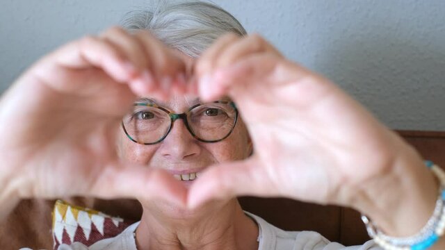 Close up of senior woman doing heart shape gesture with hands. Retired happy elderly woman making heart shape symbol with both of her hands and looking at camera
