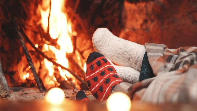 Low section legs of husband and wife covered in socks and warm blanket relaxing in front of burning fireplace during winter christmas holiday. Pair of feet in woollen socks by the Christmas fireplace
