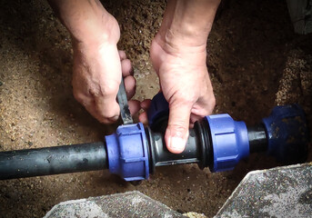 Close-up of hands fixing water pipe. Plumber fixing underground pipe with tools.