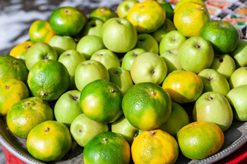 Green apples and green tangerines. Green tangerines and apples are stacked on a silver platter. Street trade. Healthy food.